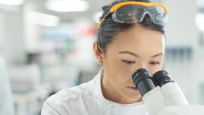 Woman in lab coat looking into a microscope